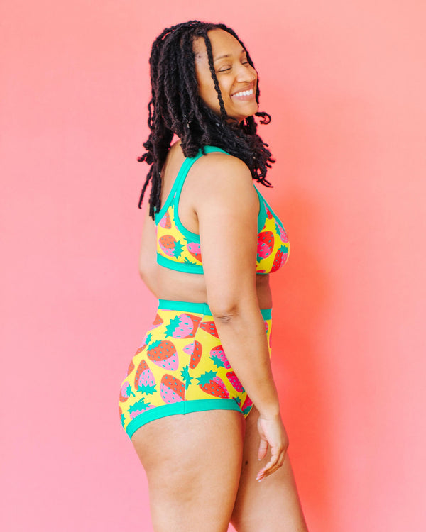 Woman wearing a colorful pineapple-patterned two-piece swimsuit against a pink background