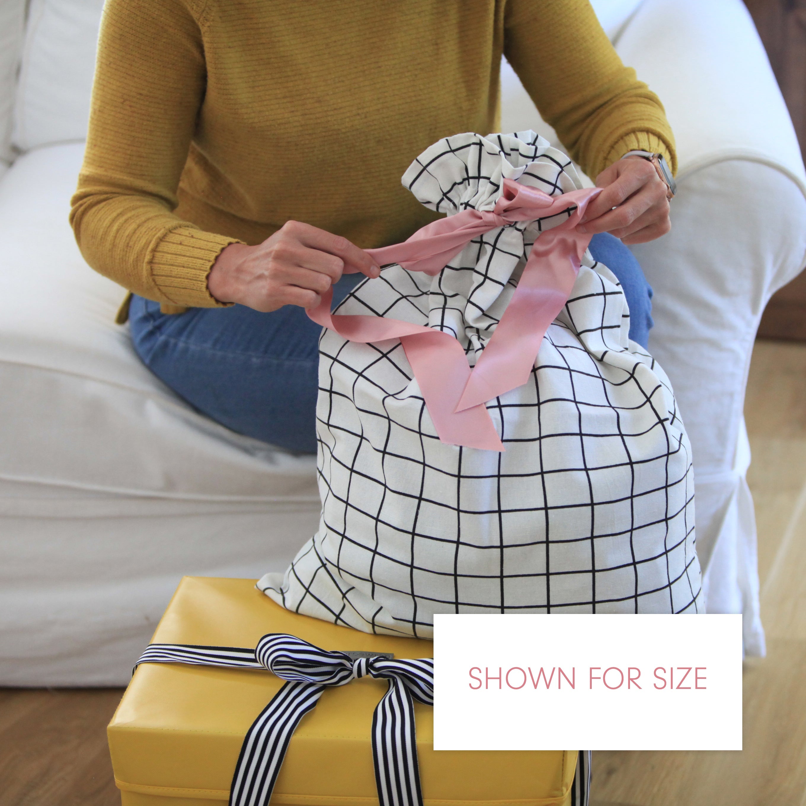 Person wrapping a gift with pink ribbon on a white couch