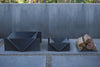 Two dark metal fire pits on a stone patio with stacked firewood against a gray wall.