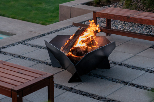 Fire pit with flames in an outdoor setting with wooden tables.