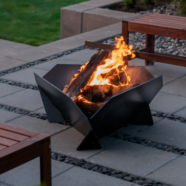 Fire pit with flames in an outdoor setting with wooden tables.