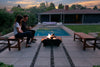 Couple sitting by a fire pit in a backyard with a pool and house in the background.