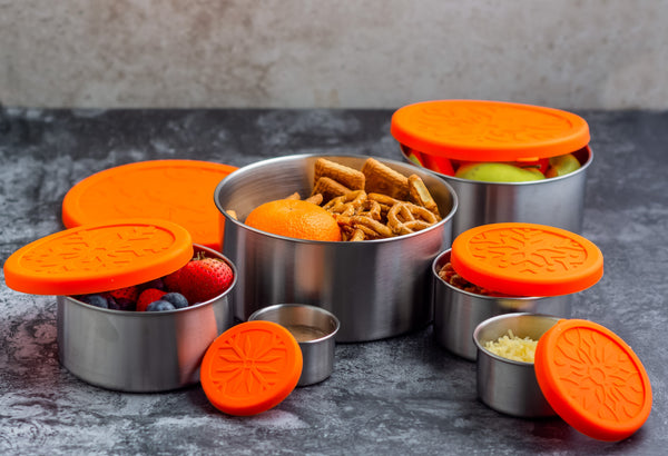 Set of stainless steel containers with orange lids on a gray surface
