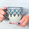 Handpainted Fair Trade stoneware coffee mug with black and blue Mayan geometric patterns, held against a textured surface