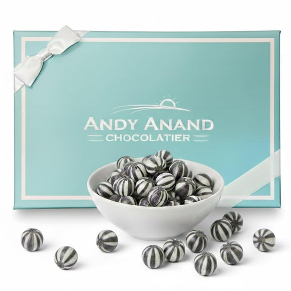 Bowl of striped chocolates in front of a turquoise box with 'Andy Anand Chocolatier' branding.