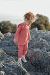 Child in a pink outfit standing on rocky terrain with trees in the background