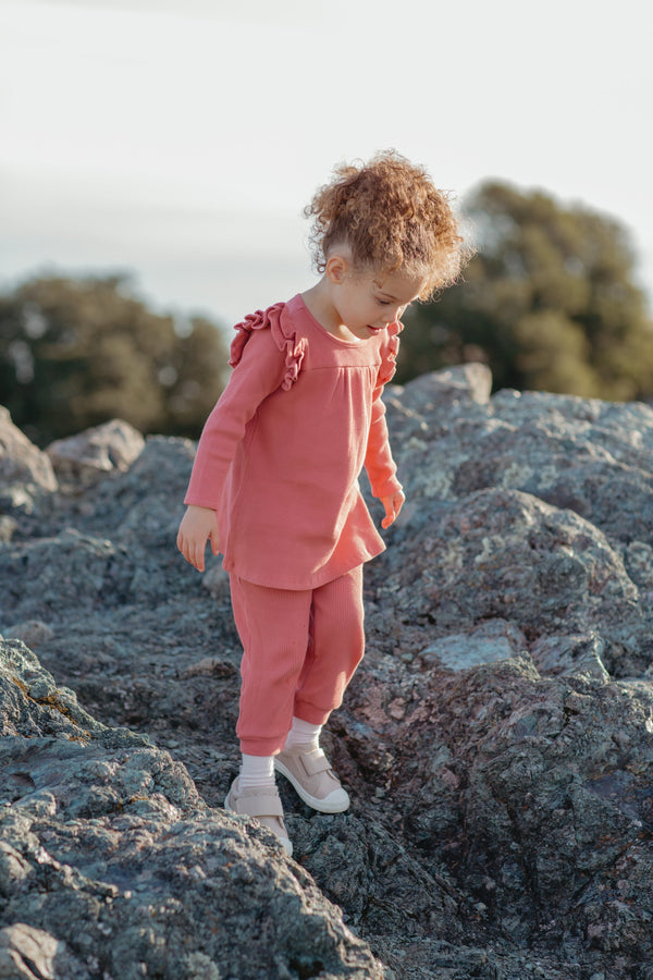 Child in a pink outfit standing on rocky terrain with trees in the background