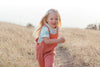 Child in pink overalls standing on a dirt path in a field