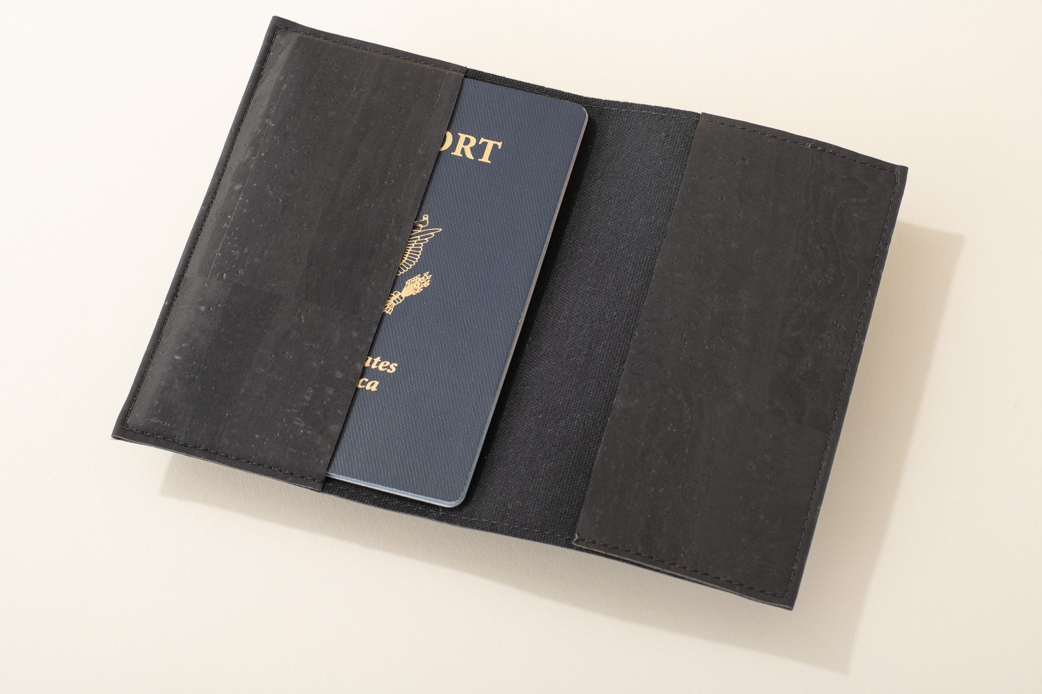 Black passport holder with a blue passport on a light beige background