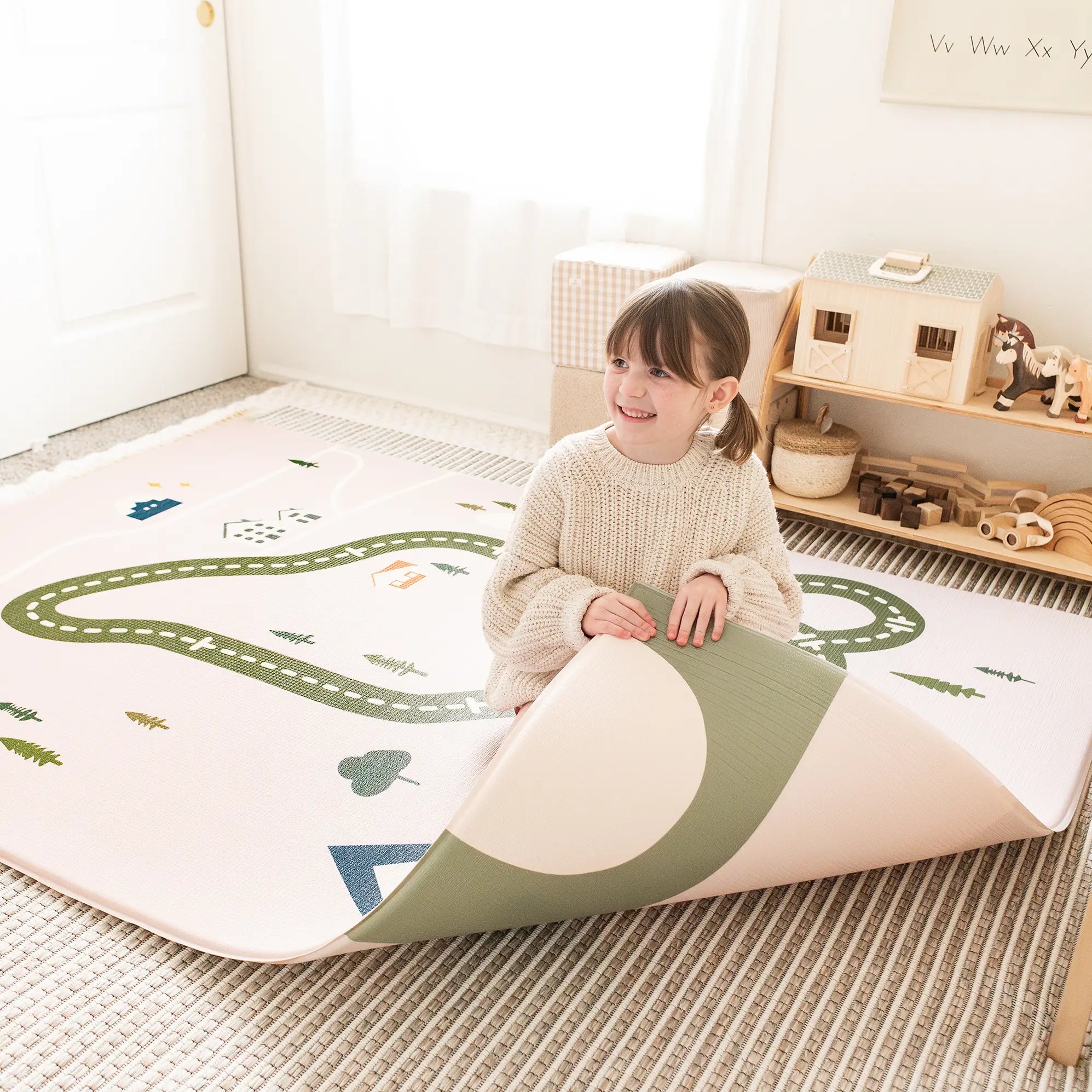 Child playing on a large play mat with road and nature designs in a room.