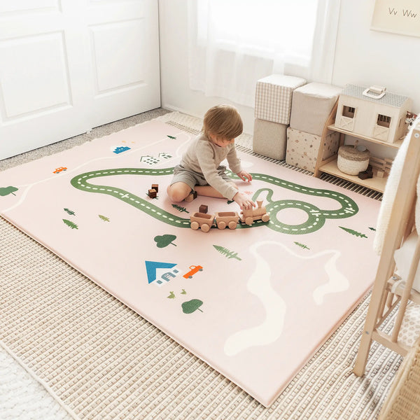Child playing with wooden train on a large play mat in a room.