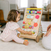 Child playing with a colorful wooden activity toy on a carpeted floor.