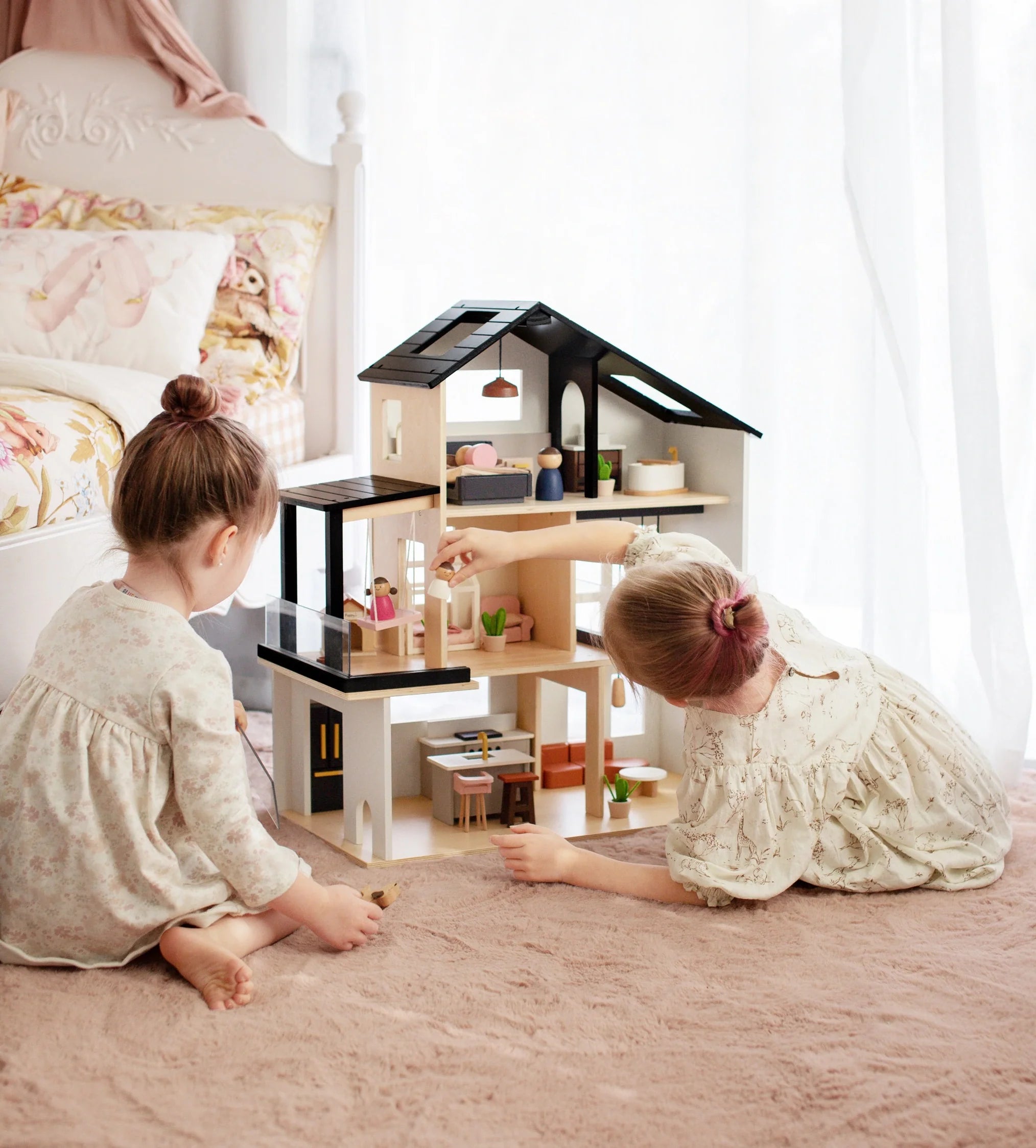 Two children playing with a dollhouse in a bright room.