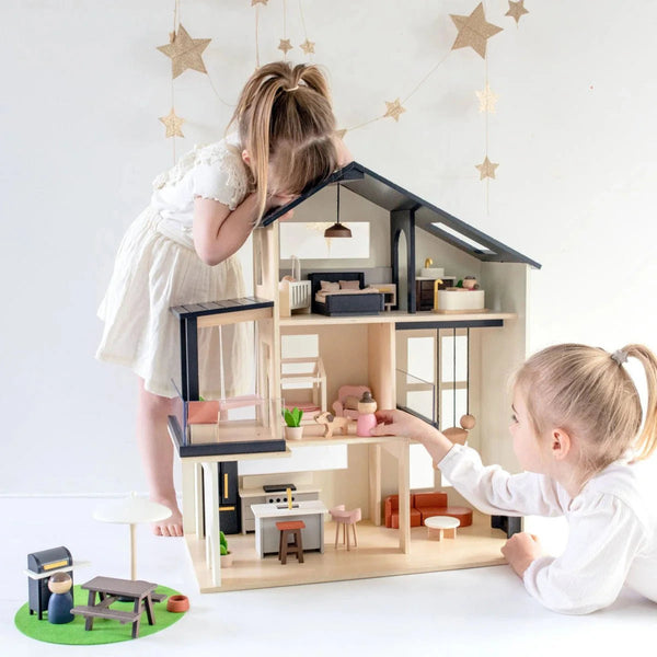 Two children playing with a dollhouse toy set on a white surface.