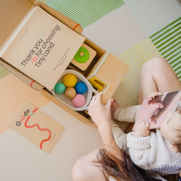 Person and child interacting with a Tinyland playset on a colorful mat