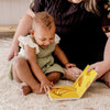 Woman and child sitting on a carpeted floor, reading a book together.