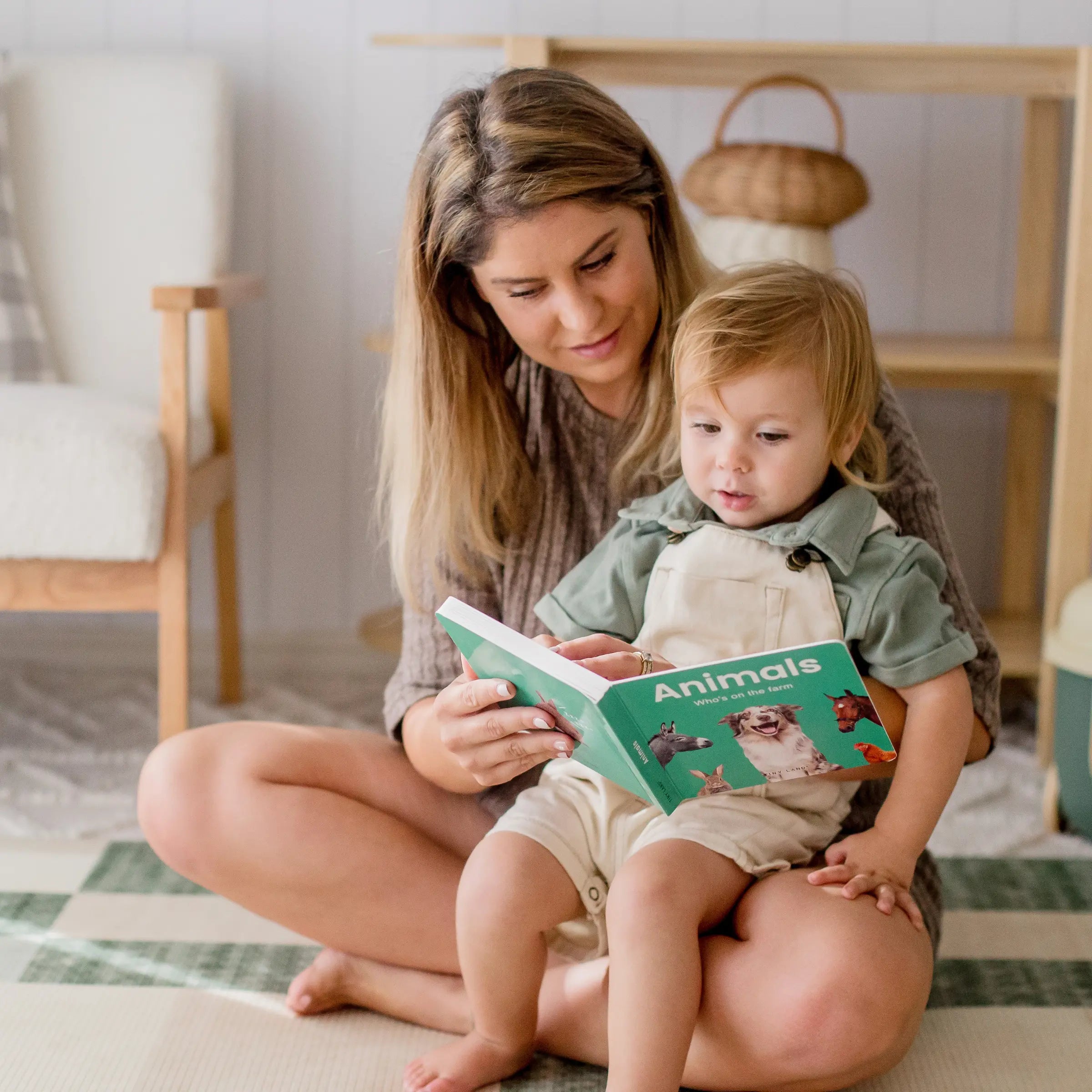 Woman reading a book titled 'Animals' to a child on the floor.