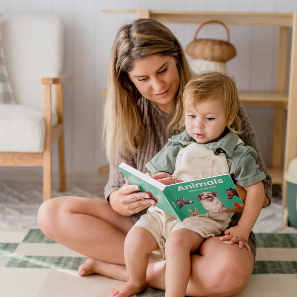 Woman reading a book titled 'Animals' to a child on the floor.