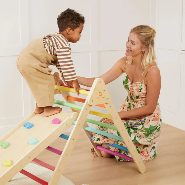 Woman and child playing with a colorful wooden climbing toy indoors.