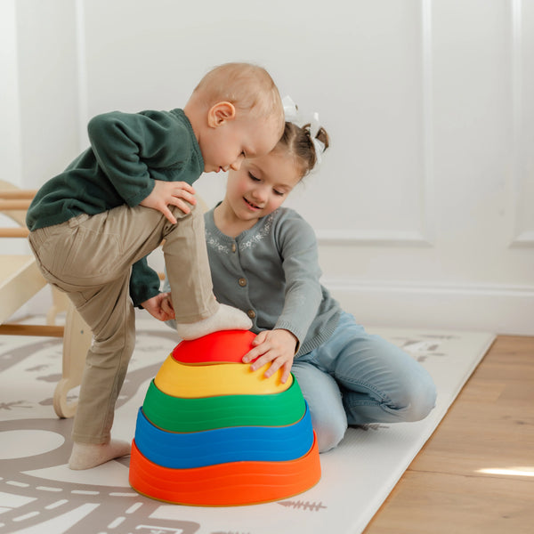 Two children playing with a colorful stacking toy on a light wooden floor.