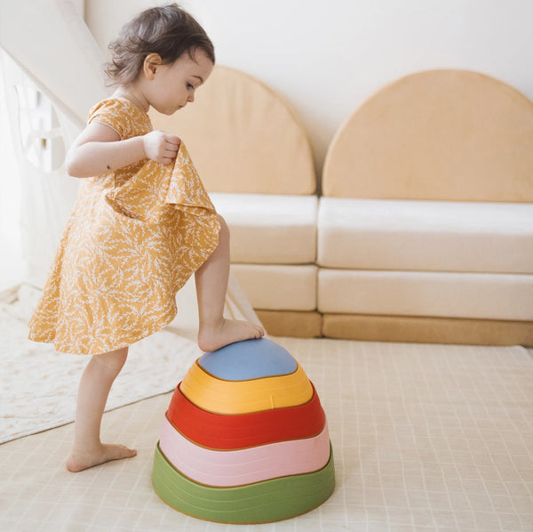 Child standing on a colorful step stool in a room with a beige sofa.