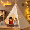 Two children inside a white teepee with string lights in a cozy room.