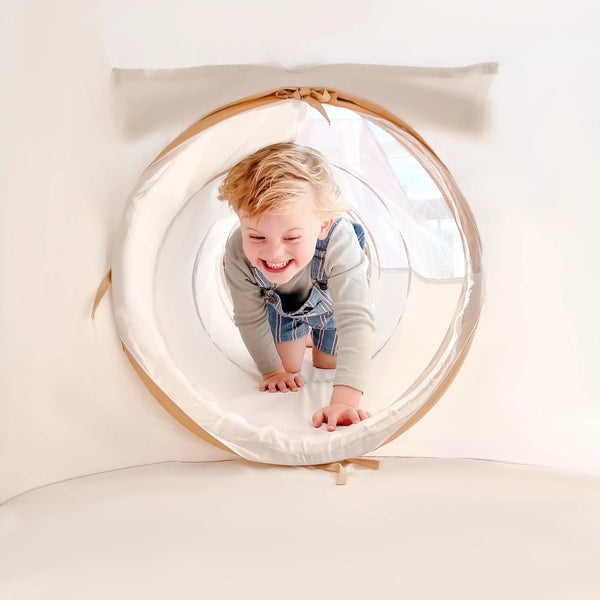 Child playing inside a transparent tunnel with beige frame on a white background