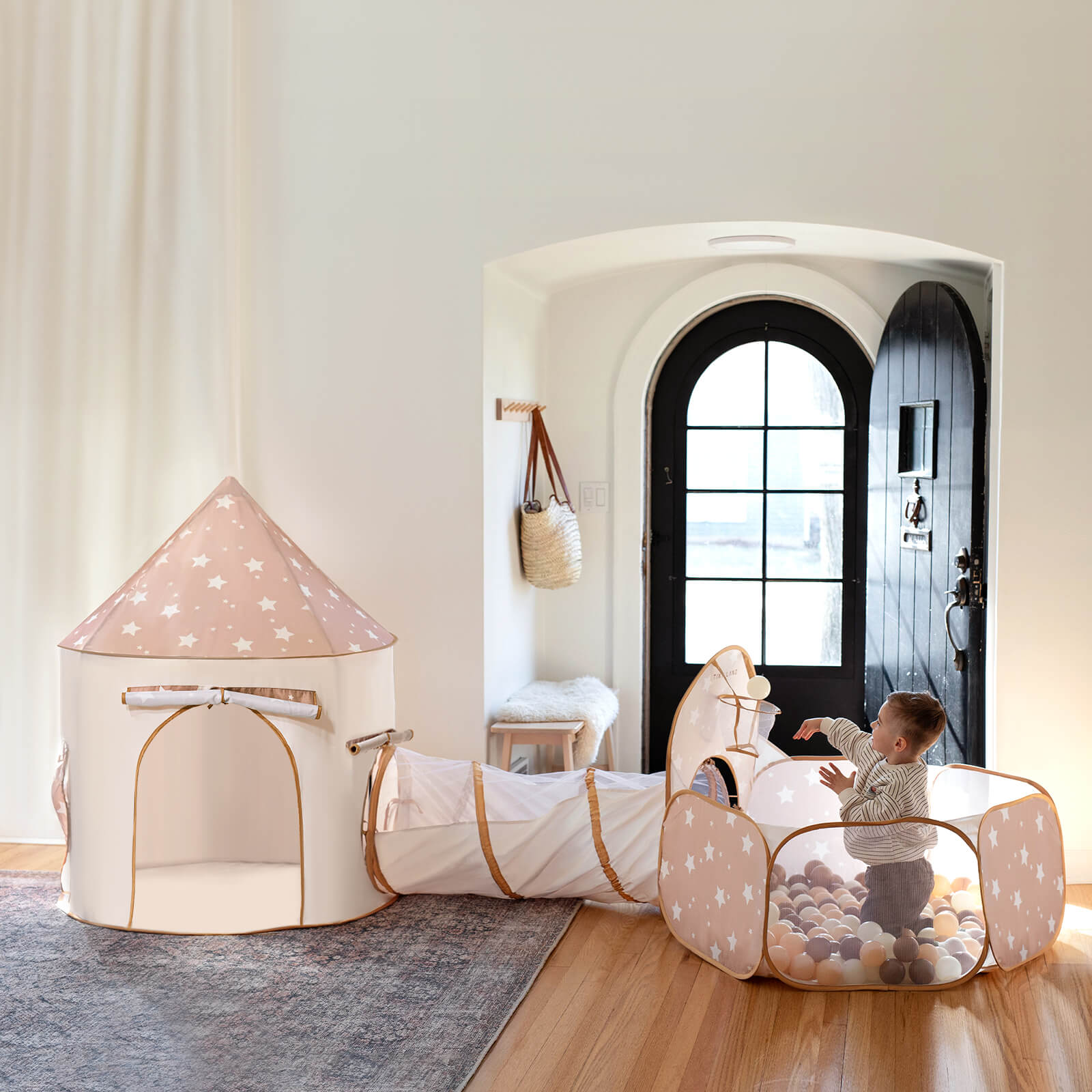 Children's play area with a pink star-patterned play tent and tunnel in a room with a black door.