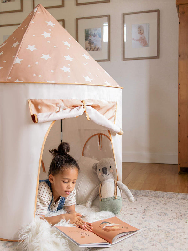 Child reading a book inside a star-patterned play tent in a cozy room.
