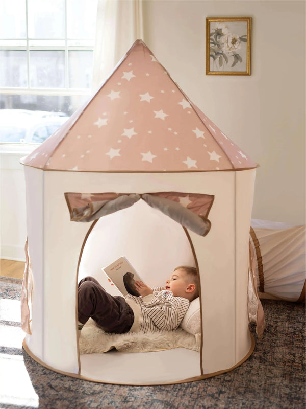 Child reading inside a star-patterned play tent in a room with a window and framed picture.