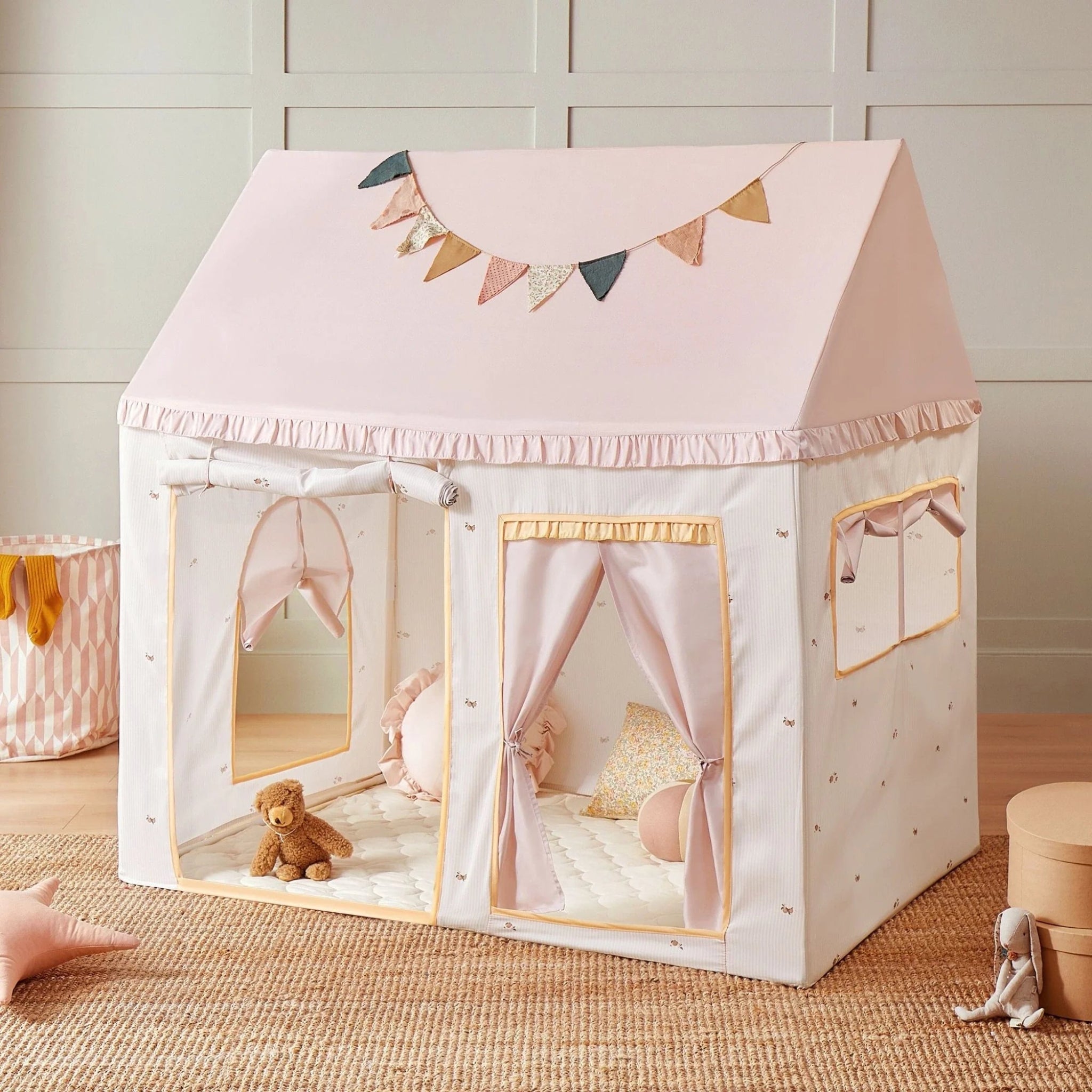 Children's play tent with pink roof and white base, decorated with a banner, on a wooden floor.
