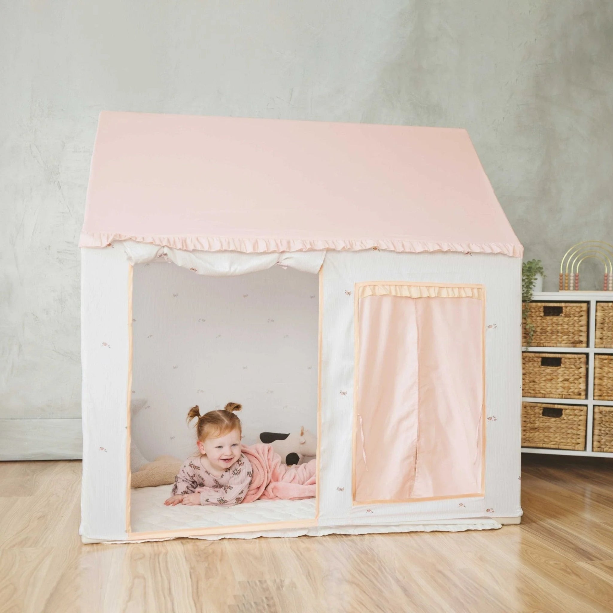 Children's playhouse with pink roof and curtains in a room setting.