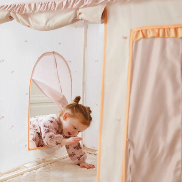 Child playing with a pink tent in a room with white walls and a window.