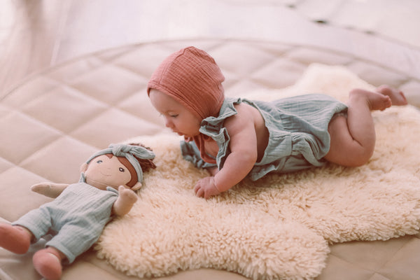 Close-up of baby in teal organic muslin romper with ruffled flutter sleeves and snap back closure