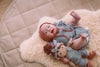 Baby wearing teal muslin flutter sleeve romper with terra cotta muslin bonnet and Paloma park friend soft toy