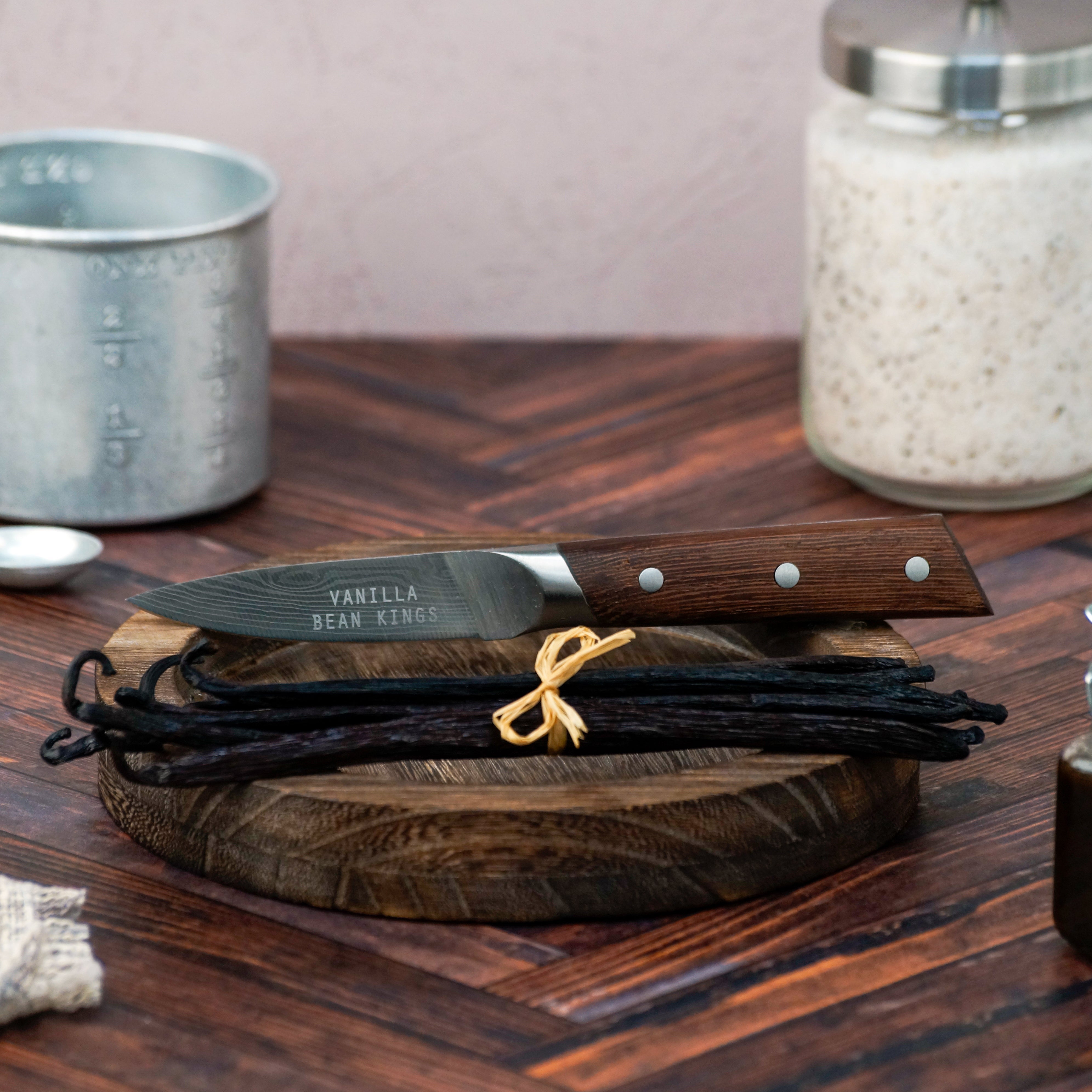 Vanilla beans and a knife on a wooden cutting board with a blurred background