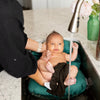 Newborn baby resting comfortably in the Teal Dream Infant Sink Bather inside a kitchen sink