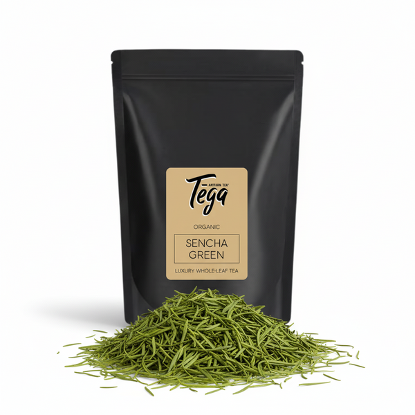 Black tea packaging with Tega Sencha Green label and loose tea leaves on a white background