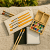Lifestyle flat lay of elseware unplug watercolor travel set open on a wooden surface with brushes and paint swatches