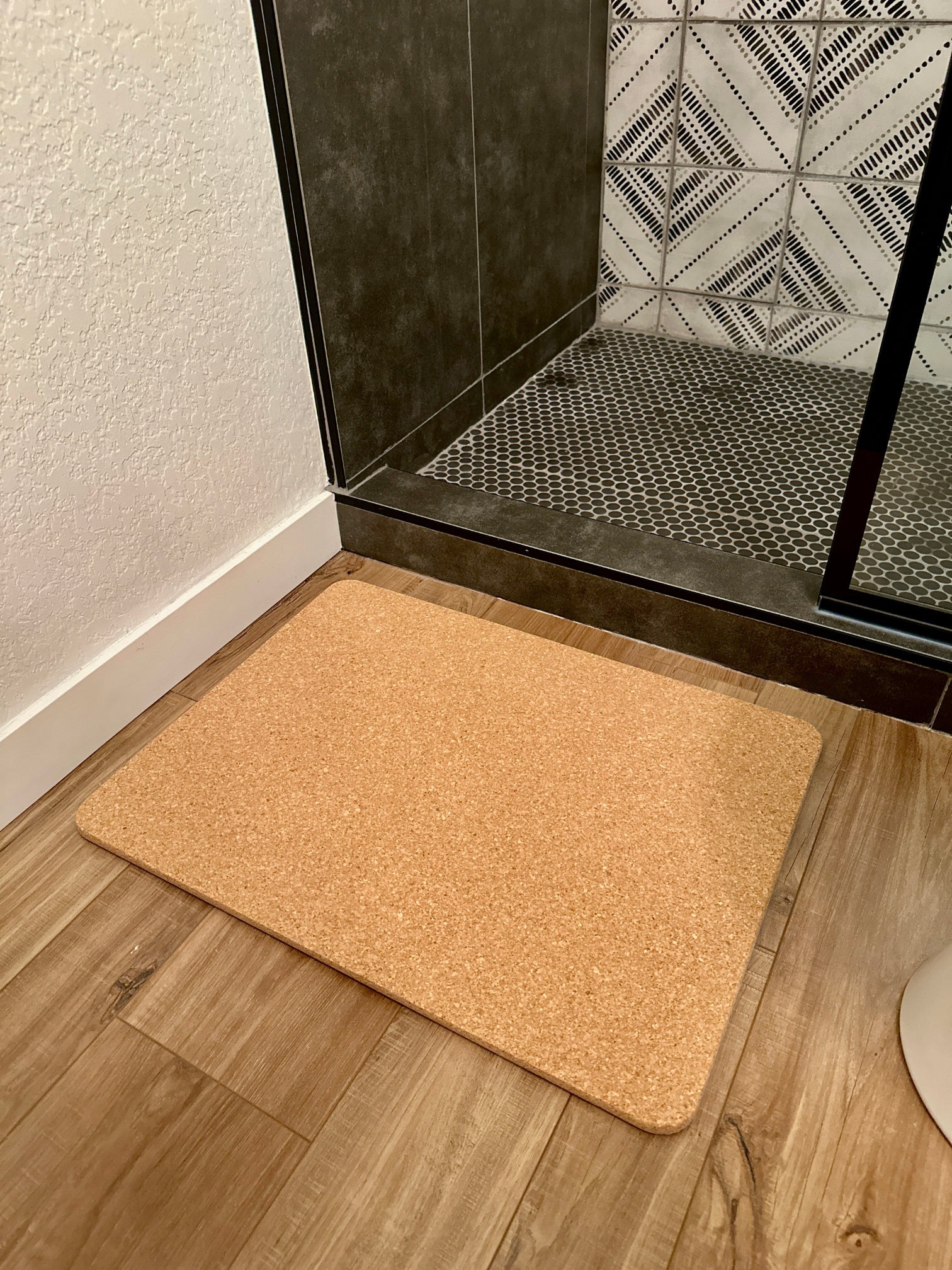 Beige cork bathroom mat on a wooden floor in front of a glass shower door.