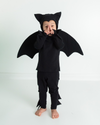 Child wearing a black bat costume on a white background