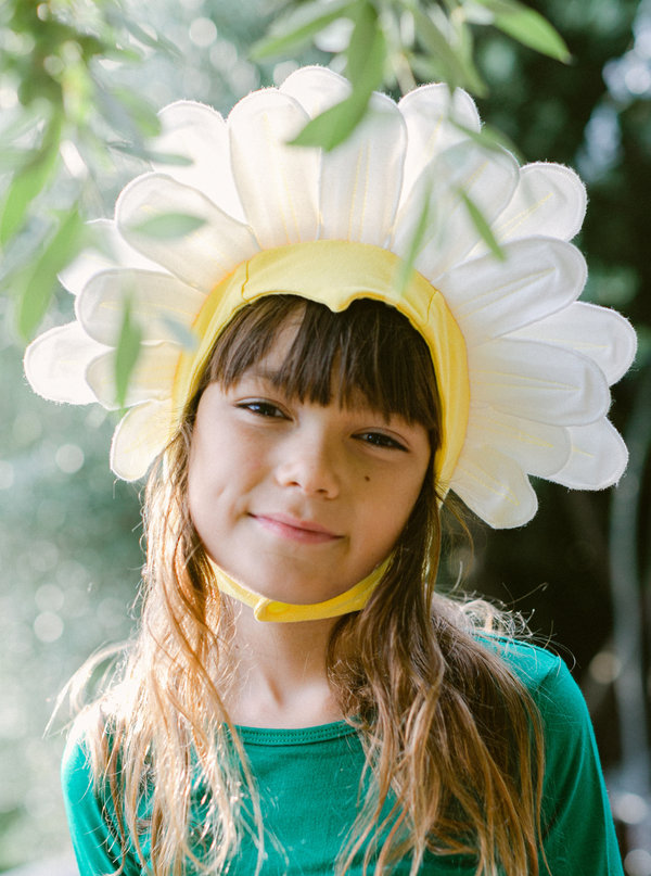 Child wearing a white flower hat with green leaves against a blurred natural background
