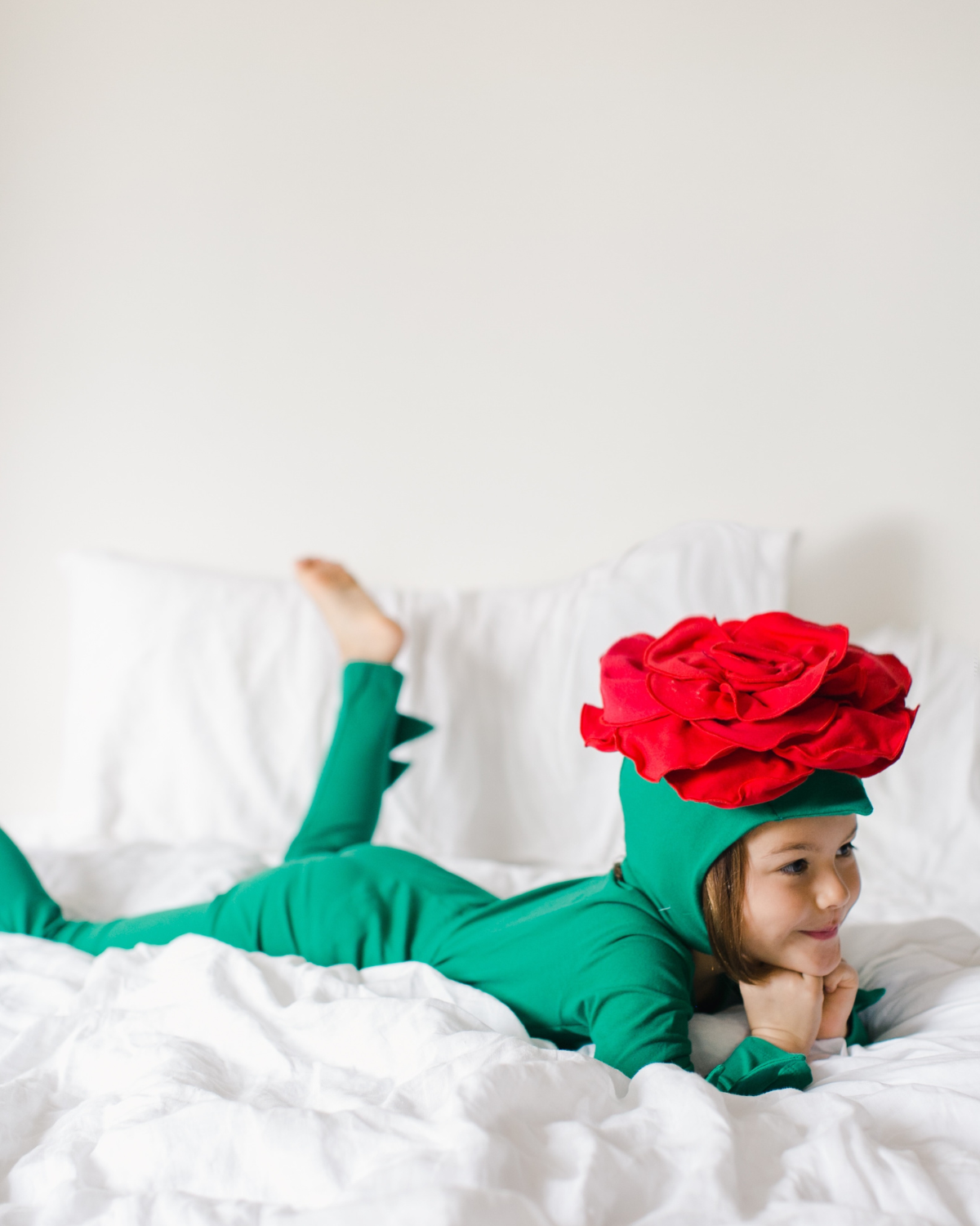 Child wearing a green dinosaur costume with a red flower on a white bed