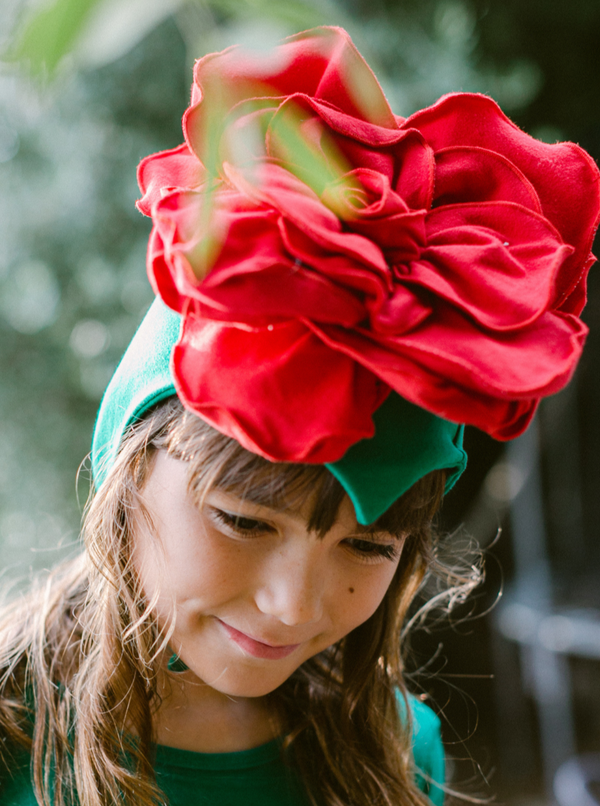 Child wearing a large red flower headband with a blurred natural background