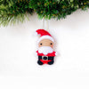 Small Santa Claus ornament hanging against a white background with greenery at the top.