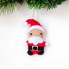 Small Santa Claus ornament hanging against a white background with greenery at the top.