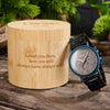 Wooden watch box with engraved message and a wooden watch on a wooden surface.