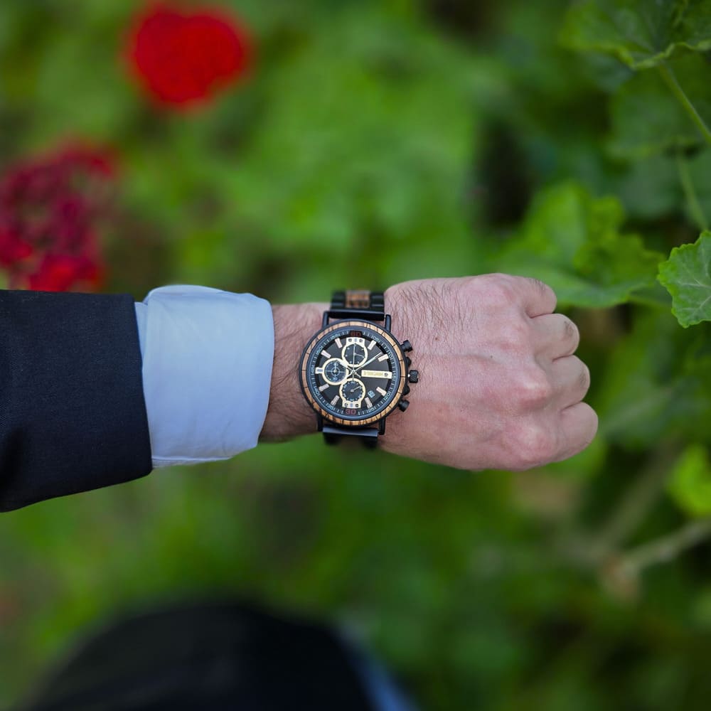 Hand wearing a wristwatch with a blurred green and red background