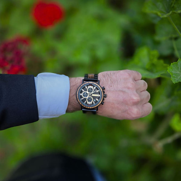 Hand wearing a wristwatch with a blurred green and red background