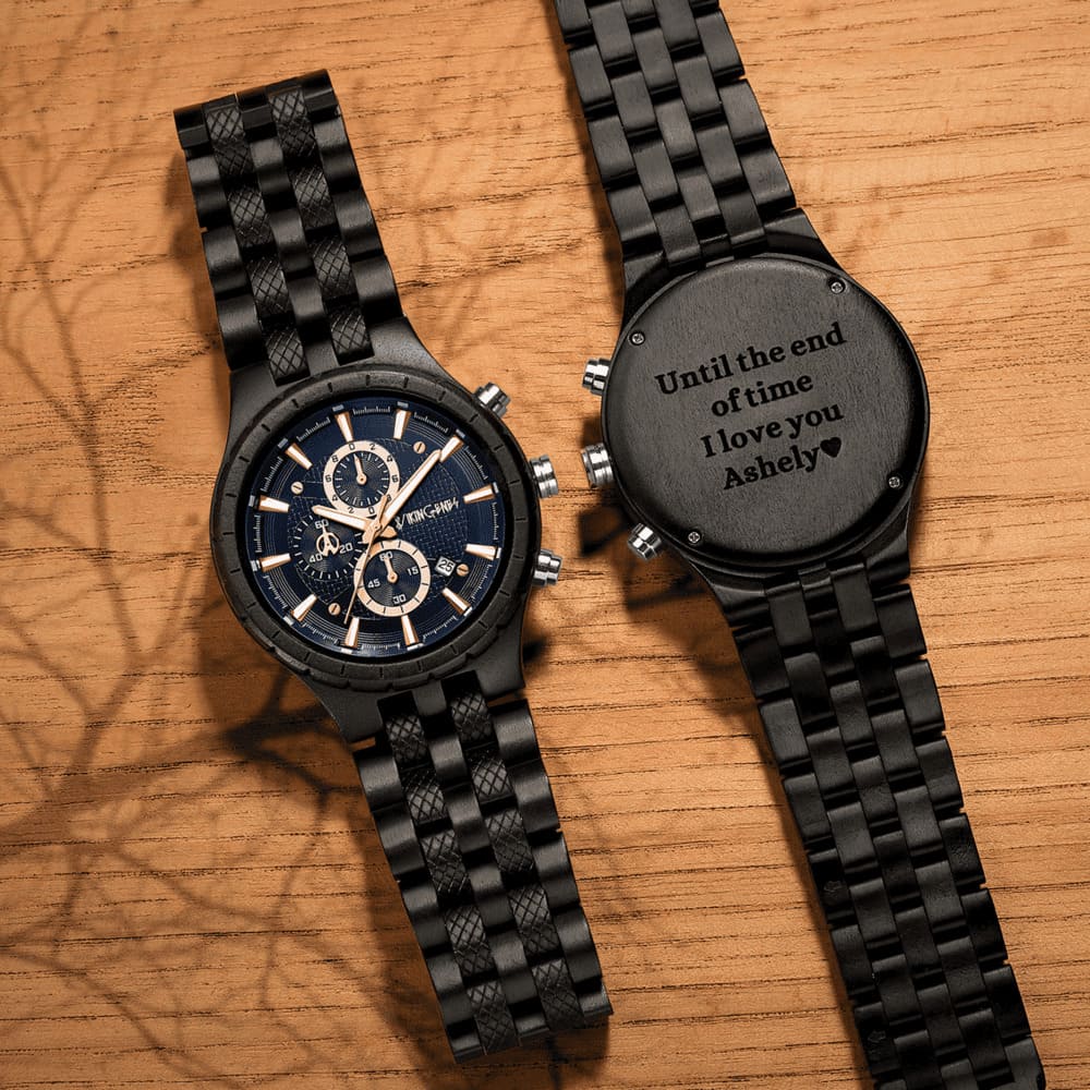 Two black watches on a wooden surface, one with engraved message.